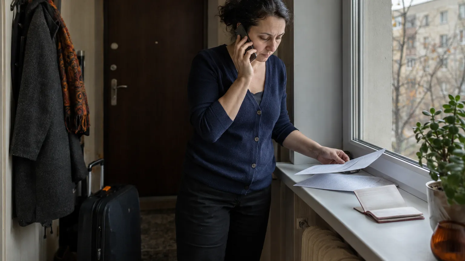 A woman by a window talks on the phone and reviews documents