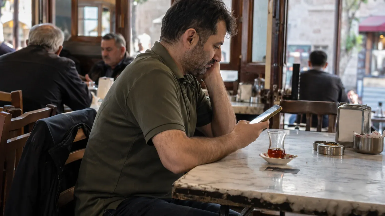 A man sitting at a cafe table looking at his smartphone