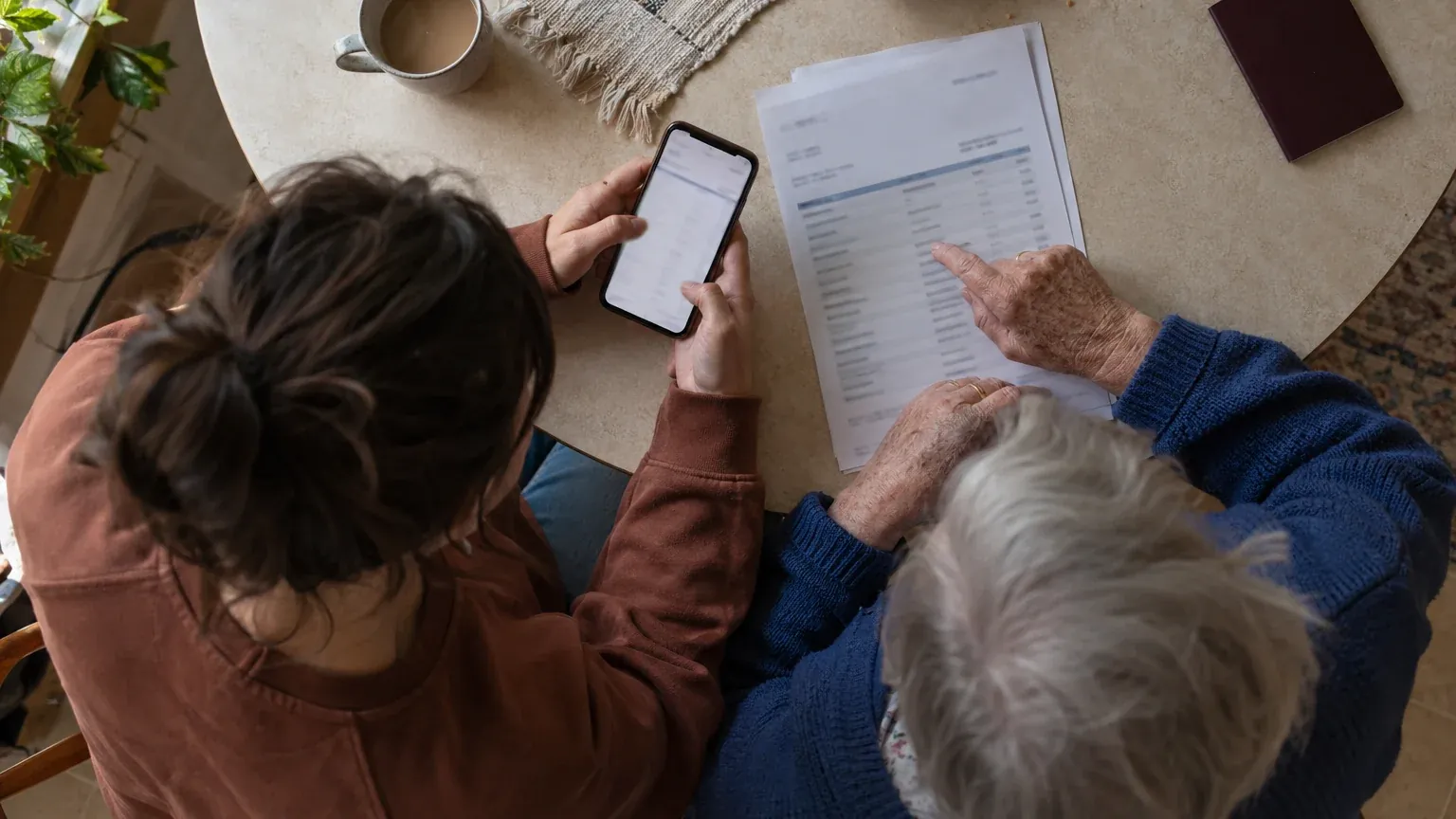 Two people at a table comparing a paper document with information on a smartphone